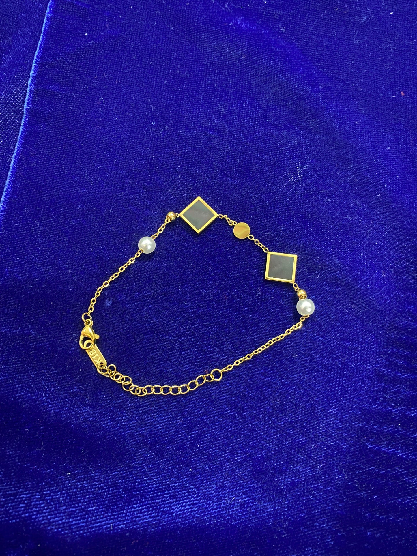 Gold bracelet with green square charms and pearls on a blue velvet background